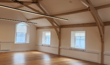 Vaulted room with timber roof trusses, arched windows and linear pendant lighting